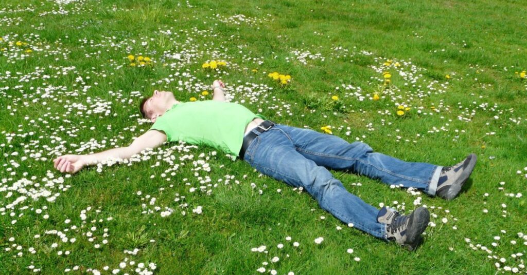 Guy in jeans sleeping outside on a grassy meadow