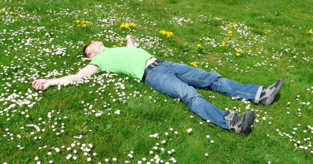 Guy in jeans sleeping outside on a grassy meadow